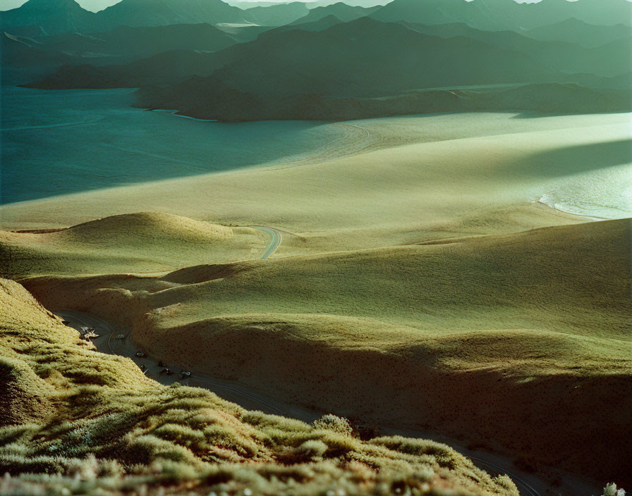 Scenic landscape: Rolling hills, winding road, tranquil lake, mountains