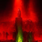 Crowd in dark space around central figure on pedestal with red lighting