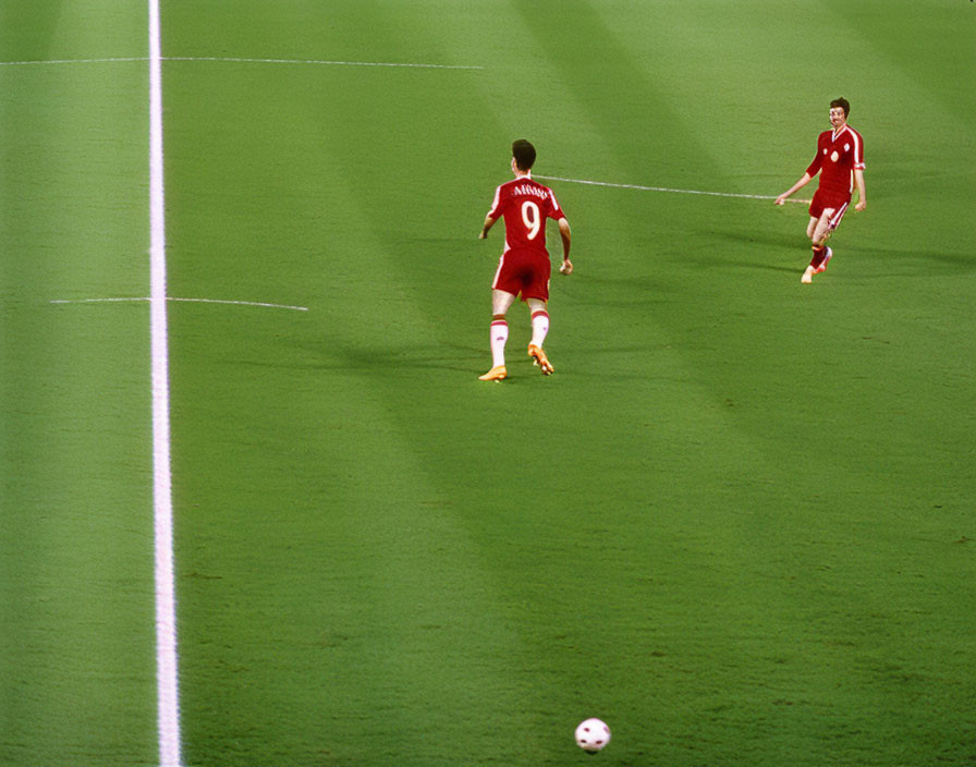 Soccer players on pitch, one chasing ball, other observing