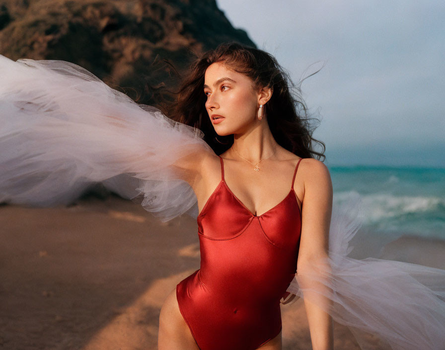 Woman in Red Swimsuit on Beach with White Fabric and Rocky Cliffs