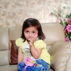 Young girl with blue eyes in yellow shawl next to colorful bird amidst delicate branches