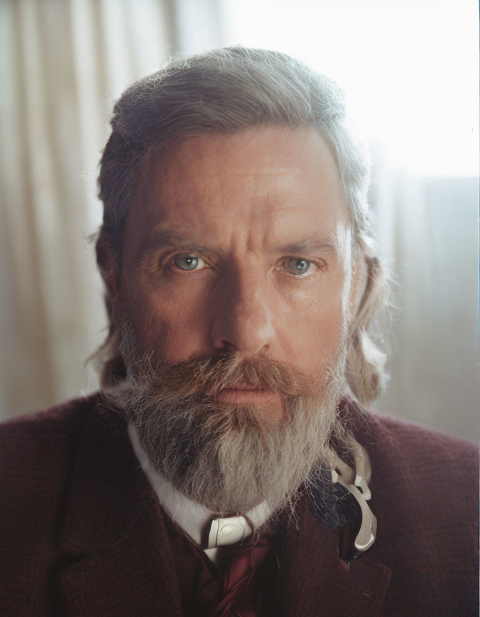 Serious man with full beard and tweed jacket, blue eyes, patterned tie