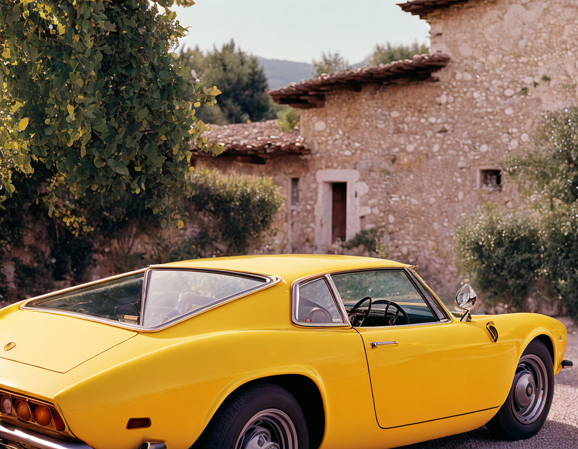 Vintage Yellow Sports Car Parked by Stone House and Greenery