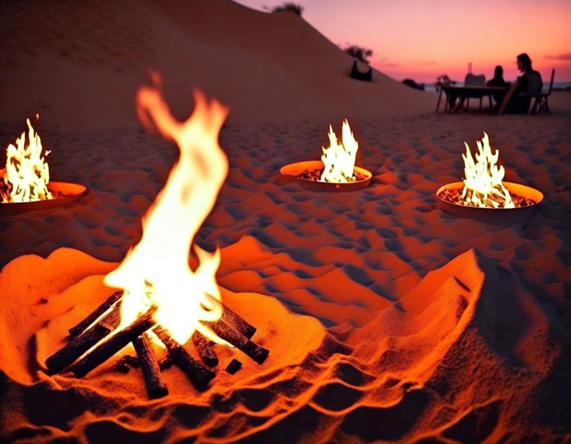 Multiple small fires in desert evening with people relaxing against dusky sky