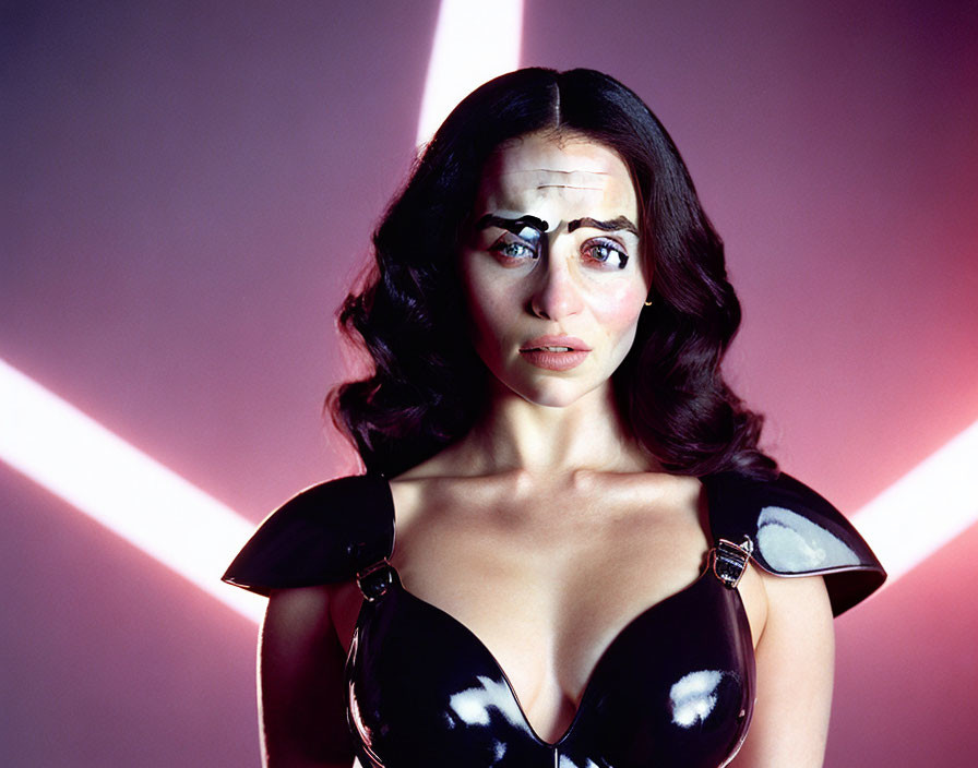 Dark-haired woman in reflective corset with teary eyes on pink background