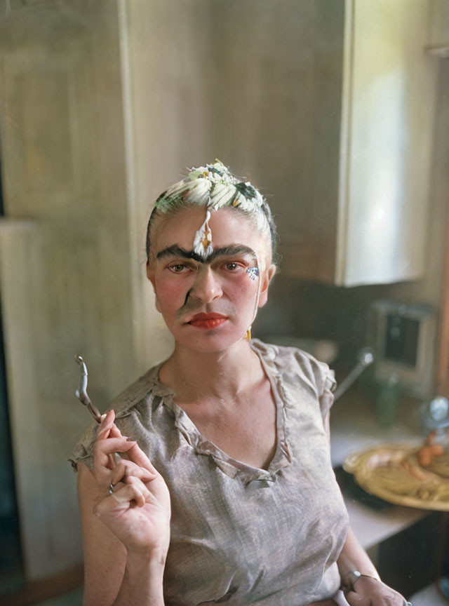 Person with dark eyebrows and red lipstick holding a paintbrush in softly lit room