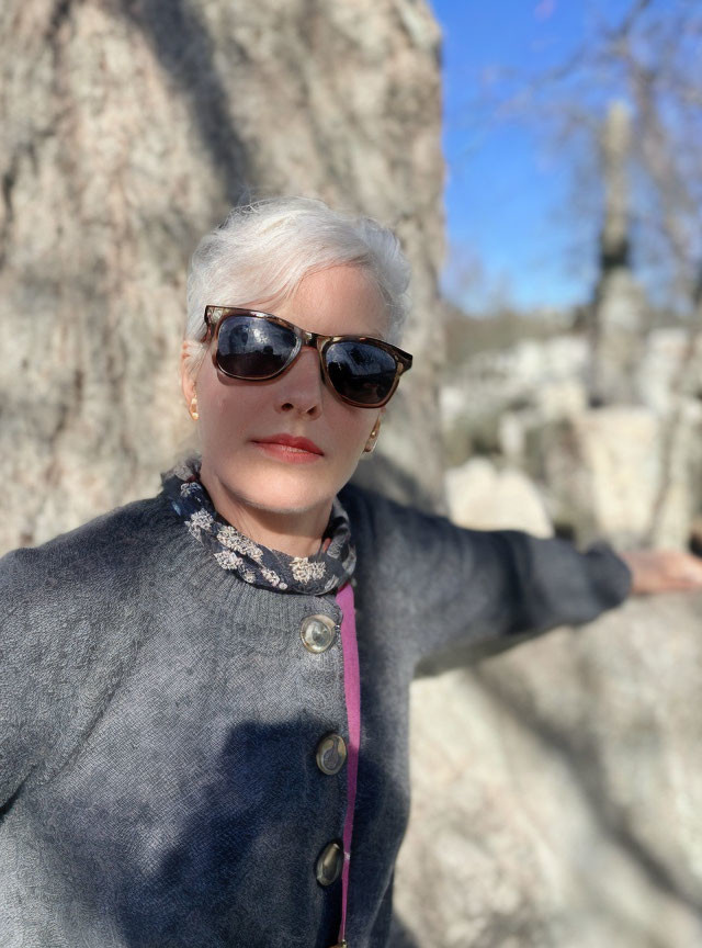 White-Haired Woman in Sunglasses Standing Against Rocky Background