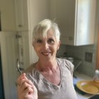 Person with dark eyebrows and red lipstick holding a paintbrush in softly lit room