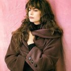 Woman with curly hair in floral coat, scarf, and earrings on pink splattered background