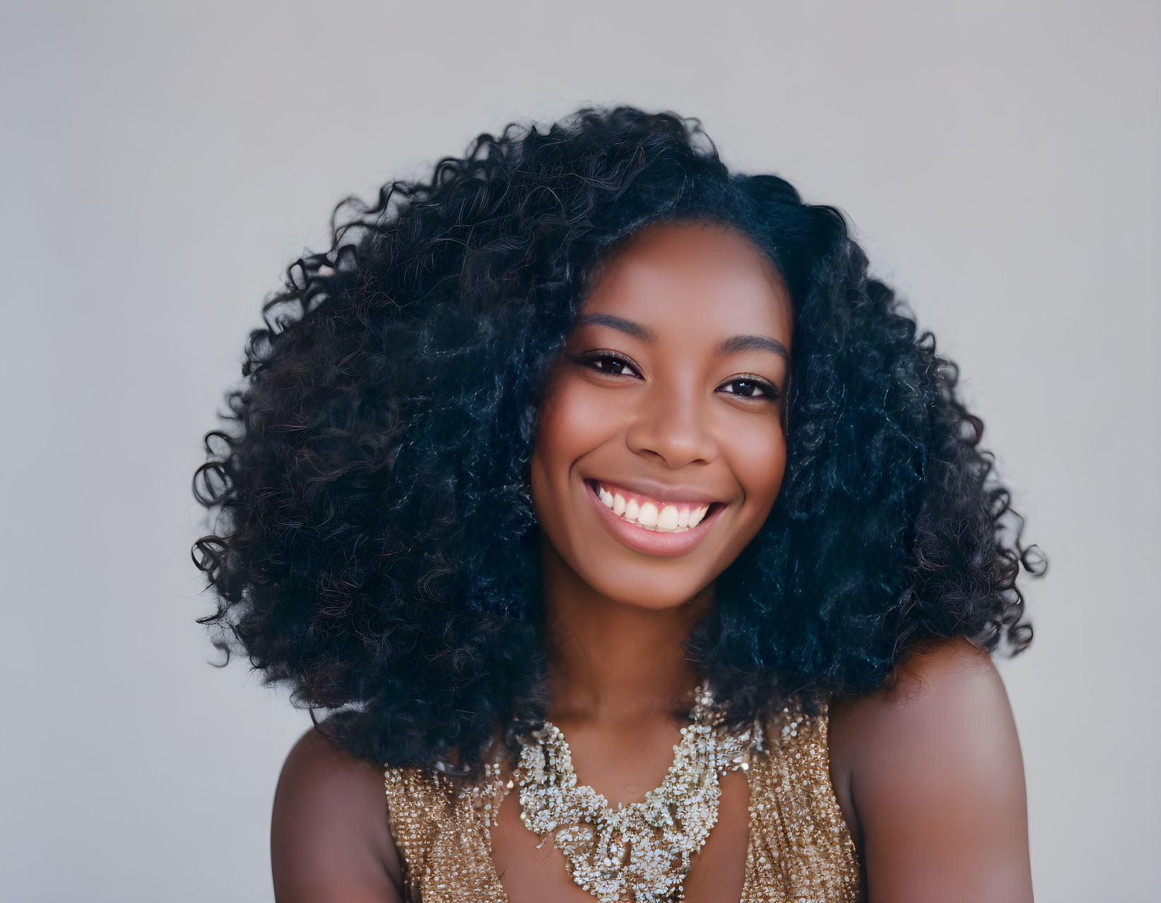 Curly-Haired Woman in Gold Top and Statement Necklace Smiling Brightly