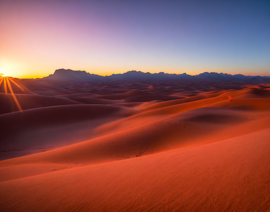 Scenic sunrise over sand dunes with mountain silhouettes