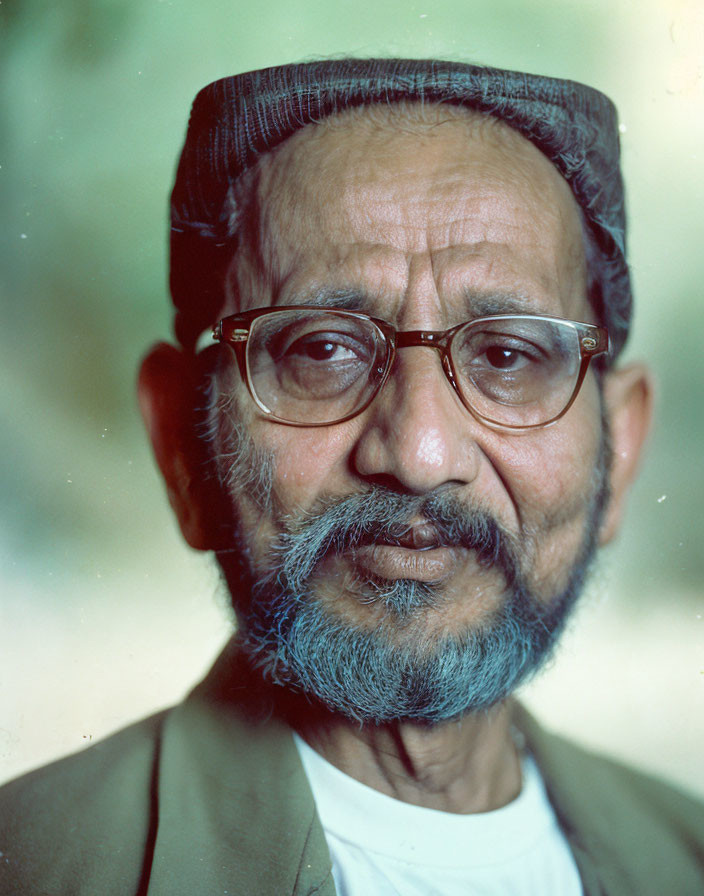 Elderly man with beard, glasses, hat, and traditional attire