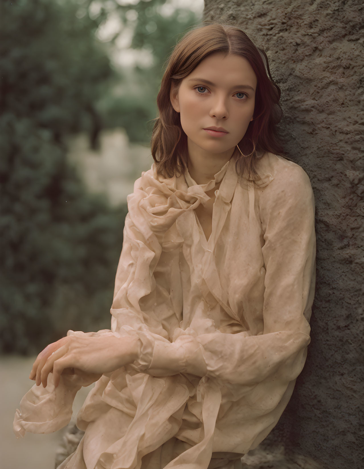 Brown-haired woman in ruffled beige blouse against stone wall