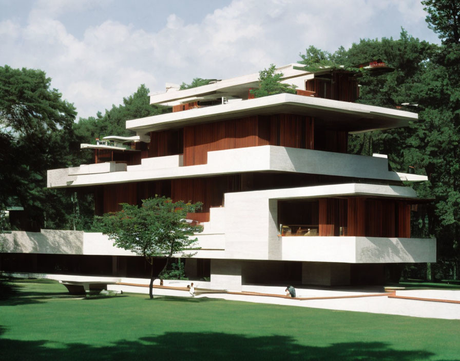 Modern multi-tiered building with flat roofs and white walls, wooden panels, surrounded by trees.