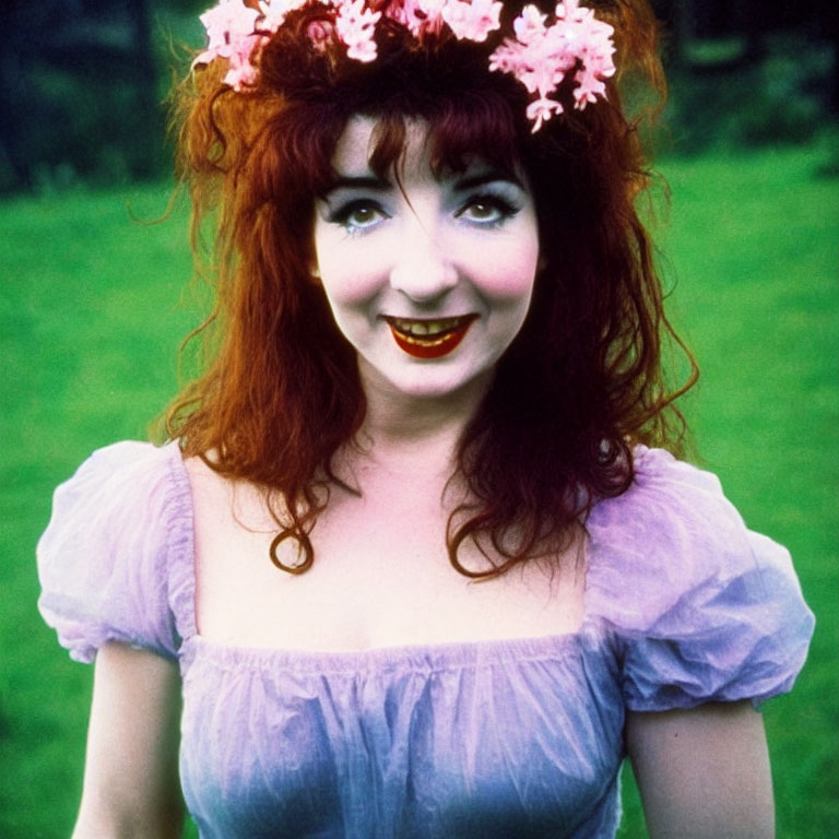 Red-haired woman in pink floral wreath and purple dress smiling outdoors.