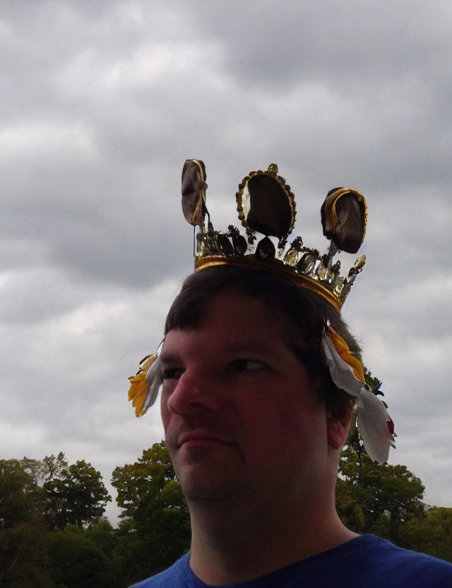 Feathered crown on person with bird figurines against cloudy sky