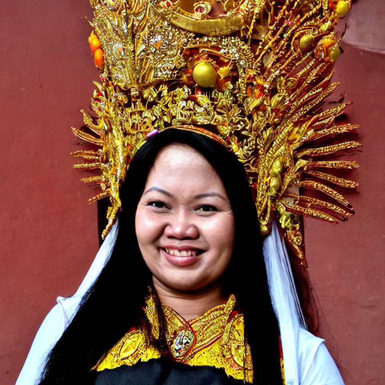 Traditional headdress adorned with gold and fruit on smiling woman against reddish-brown backdrop