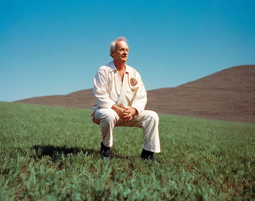 Elderly person in white karate gi and black belt on green grass