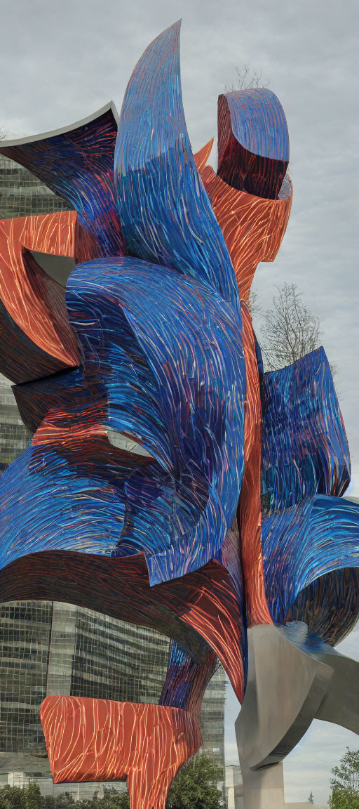 Colorful abstract outdoor sculpture with blue and red swirls among trees and building