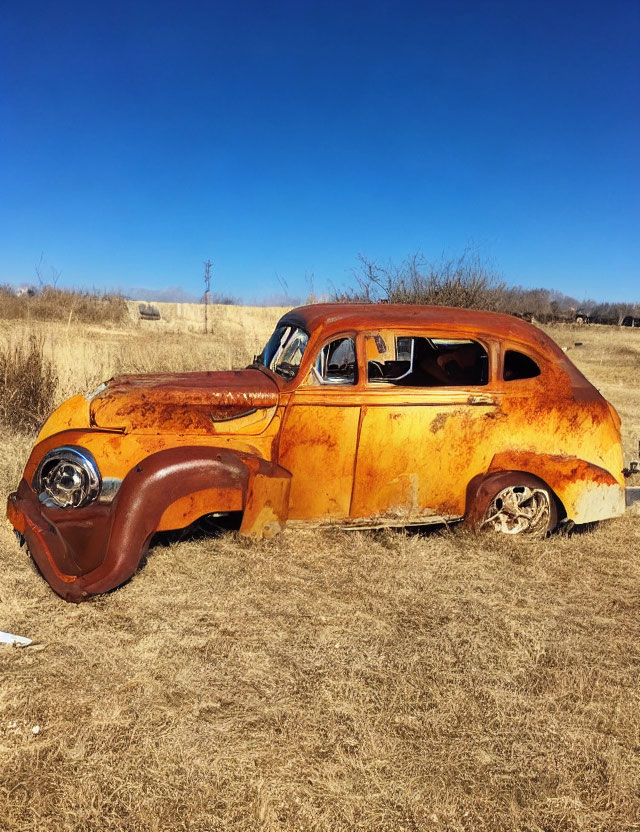 Rusted abandoned car in dry grass field under blue sky