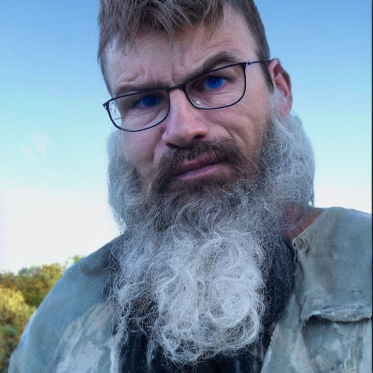 Intense man with wavy beard and glasses against blurred nature backdrop