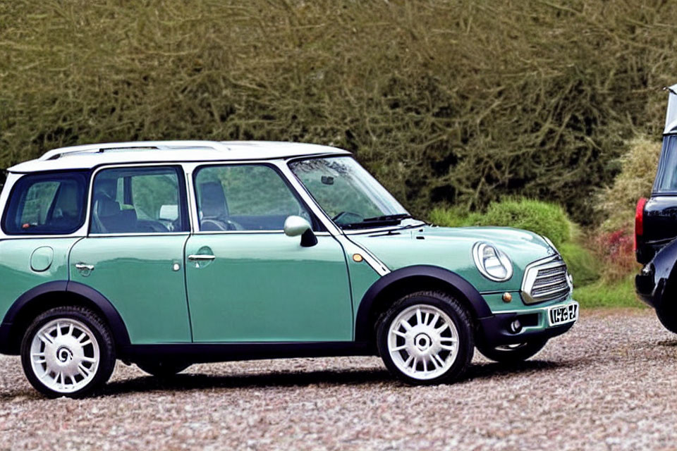 Green Mini Cooper parked on grassy area next to road with part of black vehicle visible