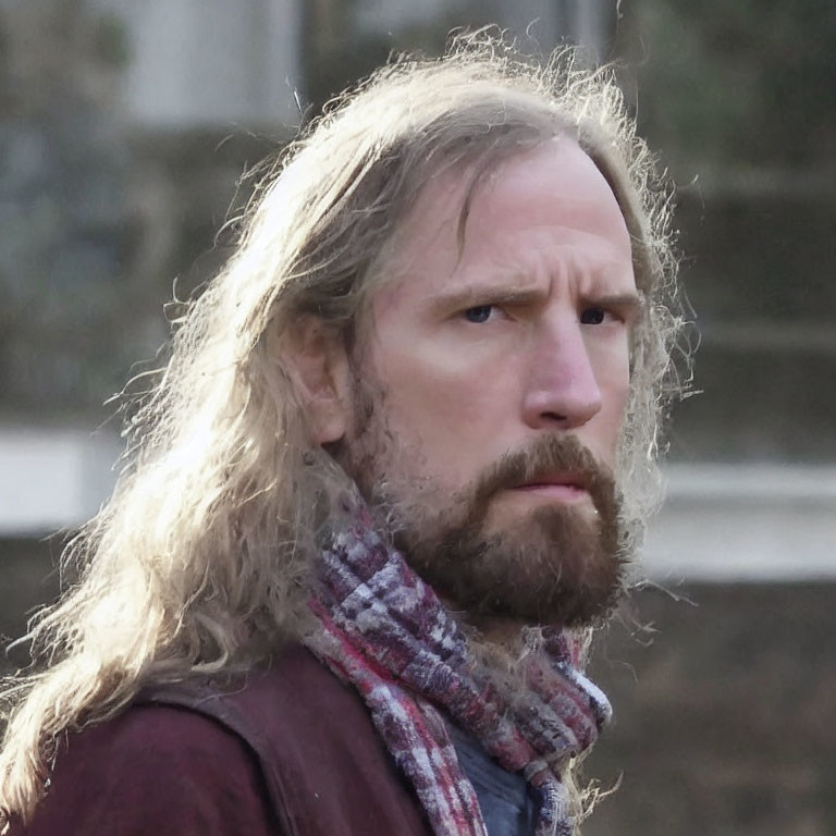 Serious man with long wavy hair in maroon jacket outdoors