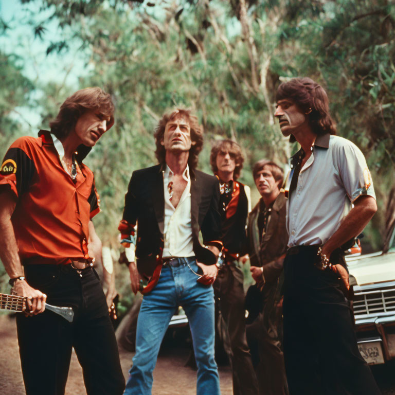 Men standing outdoors near vintage cars with forest background.