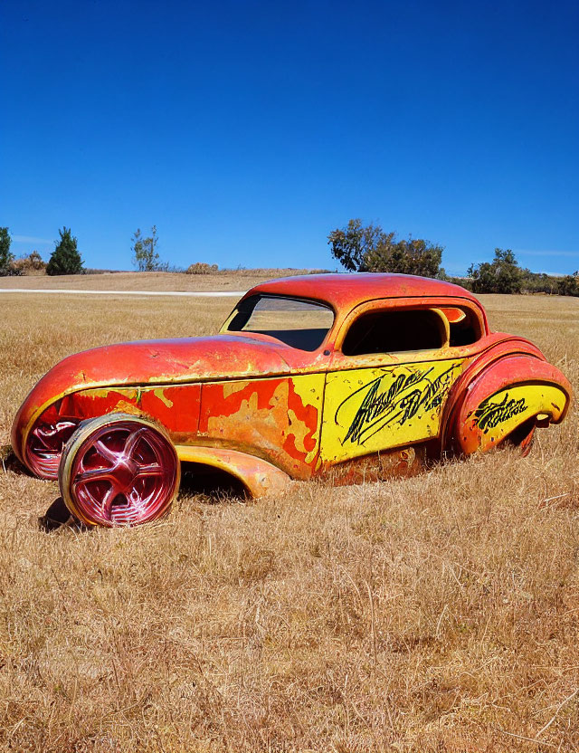 Customized vintage car with rust-like paint and flame decals in open field