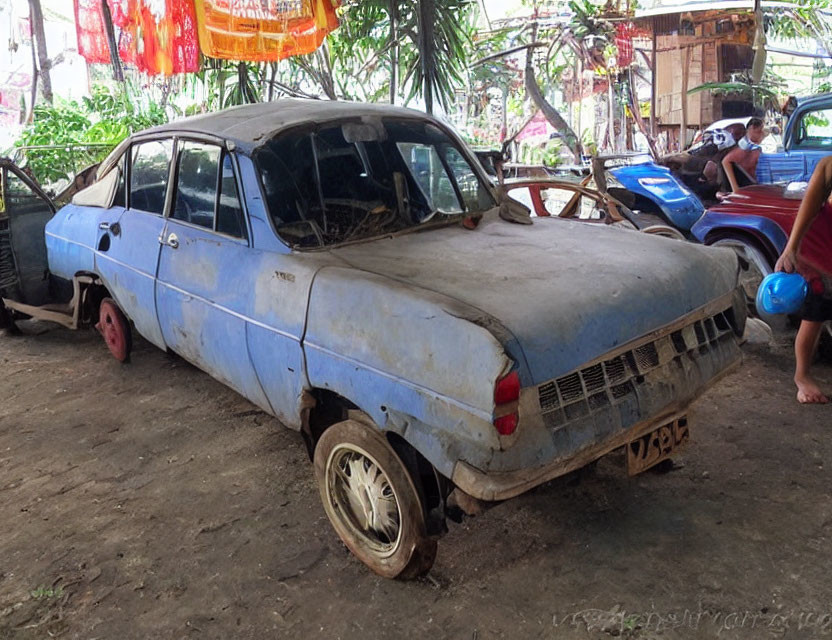 Weathered Blue Car with Missing Wheel in Tropical Setting