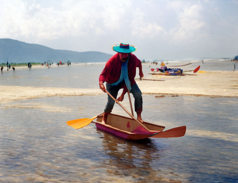 Person in red shirt paddling wooden boat near beach with people and boats.