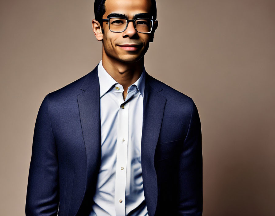 Professional smiling person in blue suit, white shirt, and glasses on brown backdrop