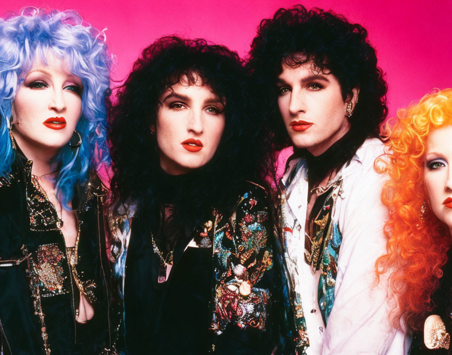 Four individuals in 80s glam rock outfits with vibrant hair and makeup on pink background