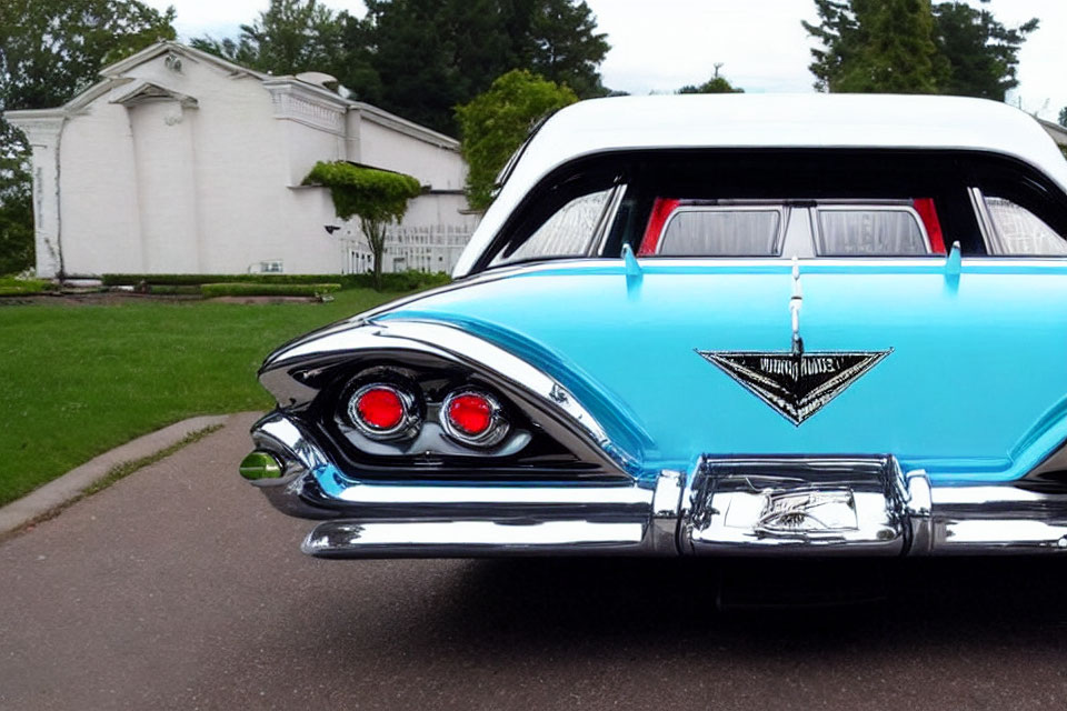 Vintage blue car with tail fins parked in front of white building with greenery