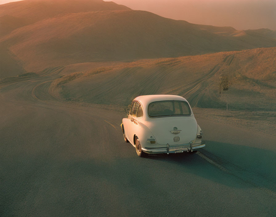 Classic White Car Drives Desert Road at Sunset