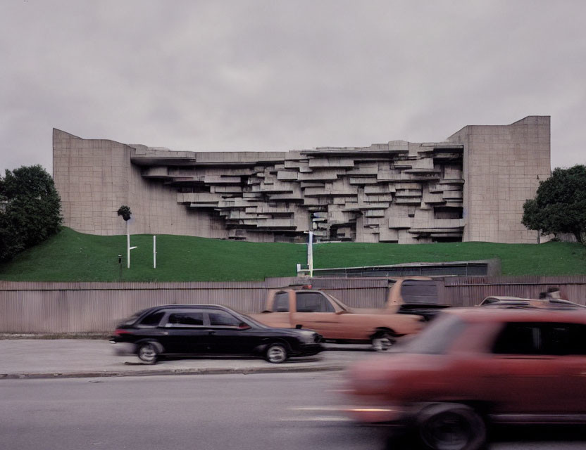 Brutalist-style building with stacked balconies and blurred cars in motion