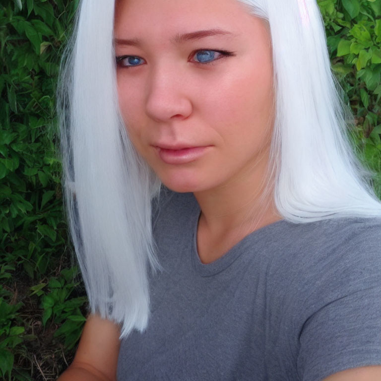 Portrait of a person with bright blue eyes and white hair on green leafy backdrop