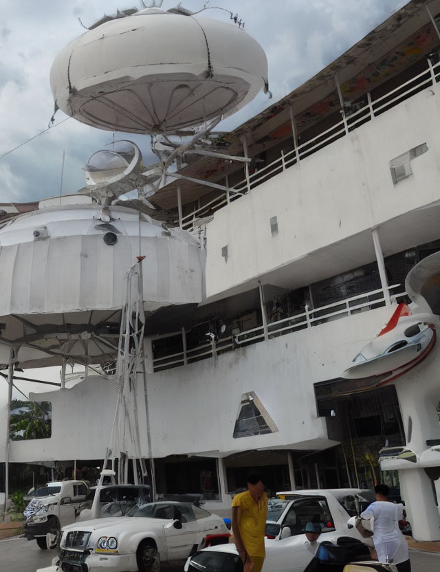 Multi-story building with satellite dish, antennas, cars, and person.