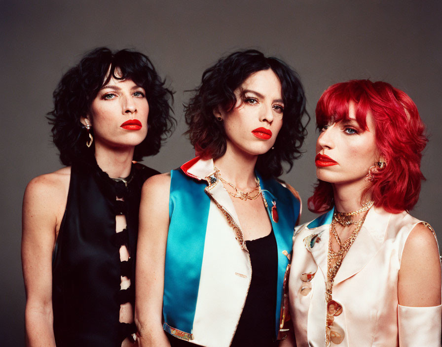 Three women with red lipstick and wavy hair in elegant outfits posing confidently