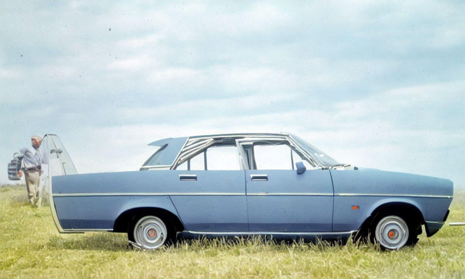 Vintage Blue Sedan Parked on Grass with Man Walking Towards Ladder under Cloudy Sky