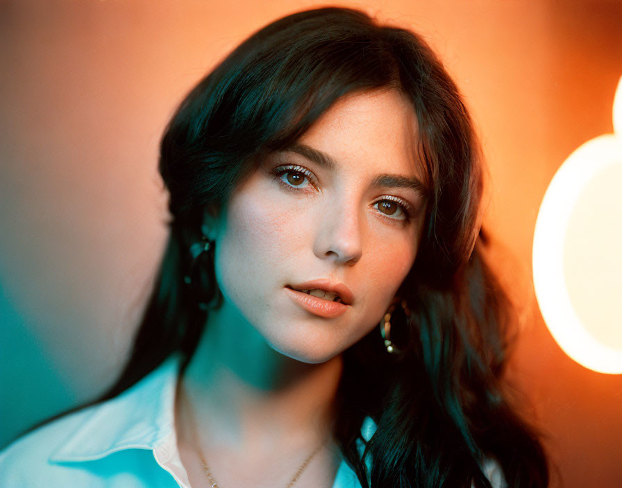 Dark-haired woman in white shirt and earrings under dual-tone lighting