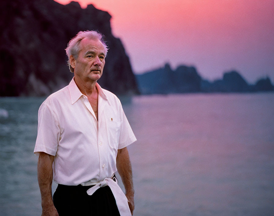 Elderly man with gray hair on beach at dusk with pink and purple sky