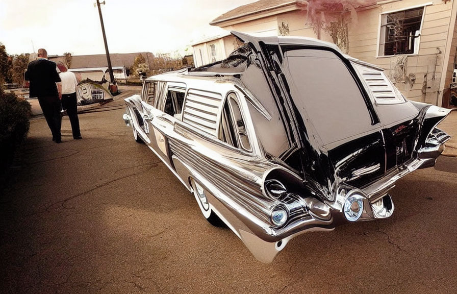 Vintage black hearse with chrome details parked, two people under hazy sky