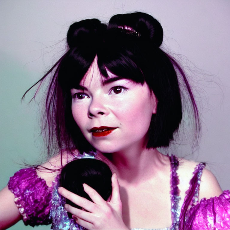 Dark-haired woman in sparkly purple attire holding black object on pastel background