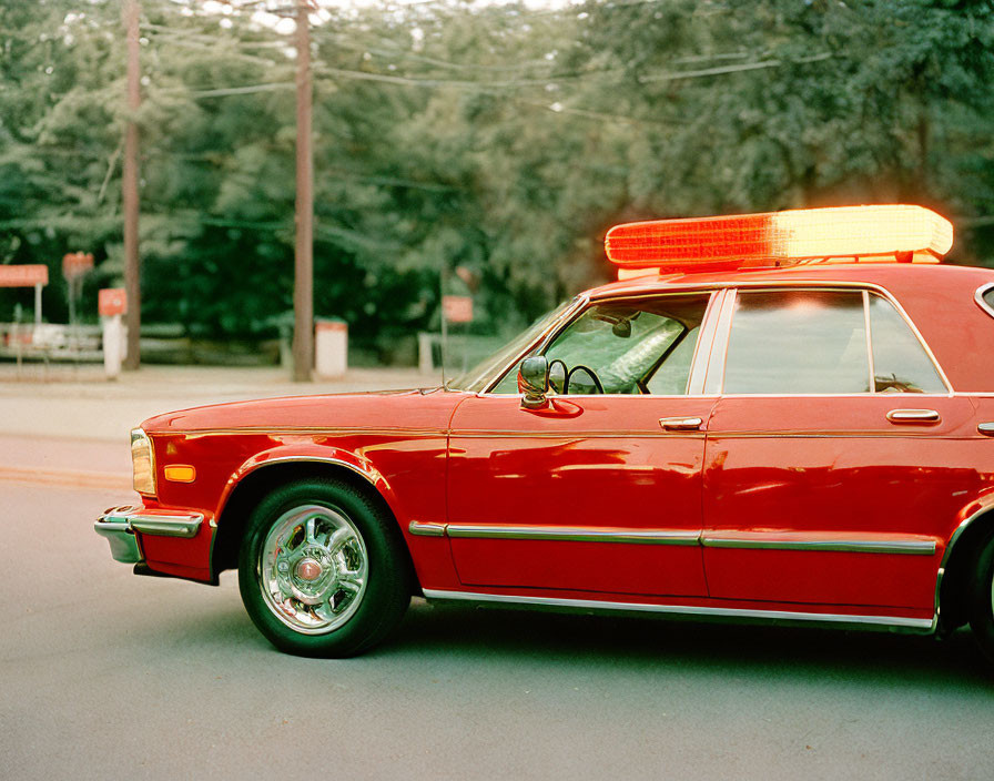 Vintage Red Police Car with Flashing Light Bar Parked Near Road