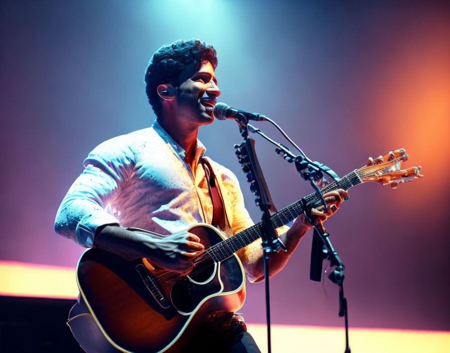 Musician performs acoustic guitar and sings under warm purple and yellow stage lights