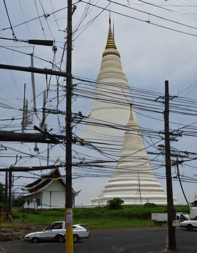 Buddhist stupa with power lines, car, and building in scene