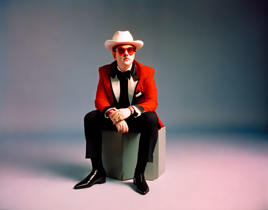 Person in Red Suit Jacket on Gray Cube in Blue Studio