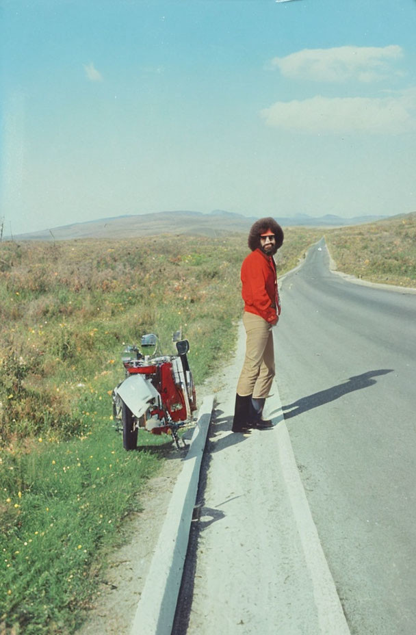 Person with Afro Hairstyle Next to Motorcycle on Open Road