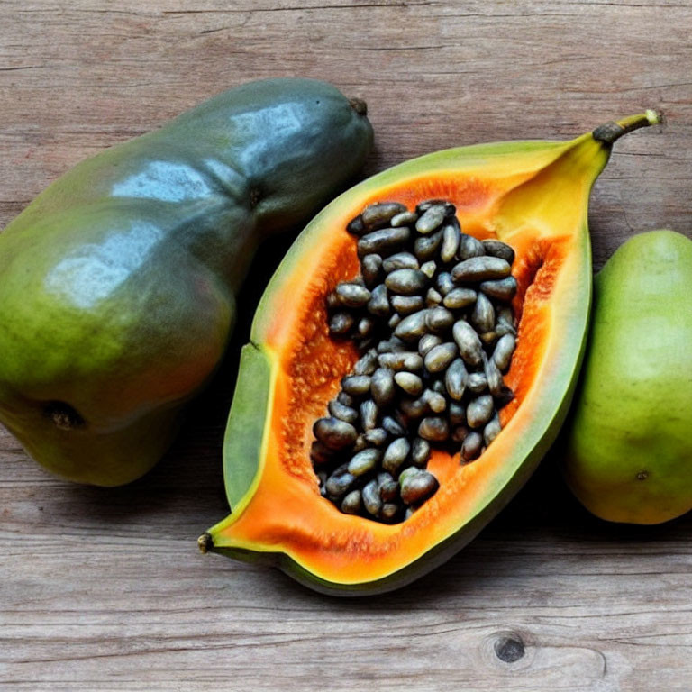 Fresh Papaya Whole and Sliced with Black Seeds on Wooden Surface